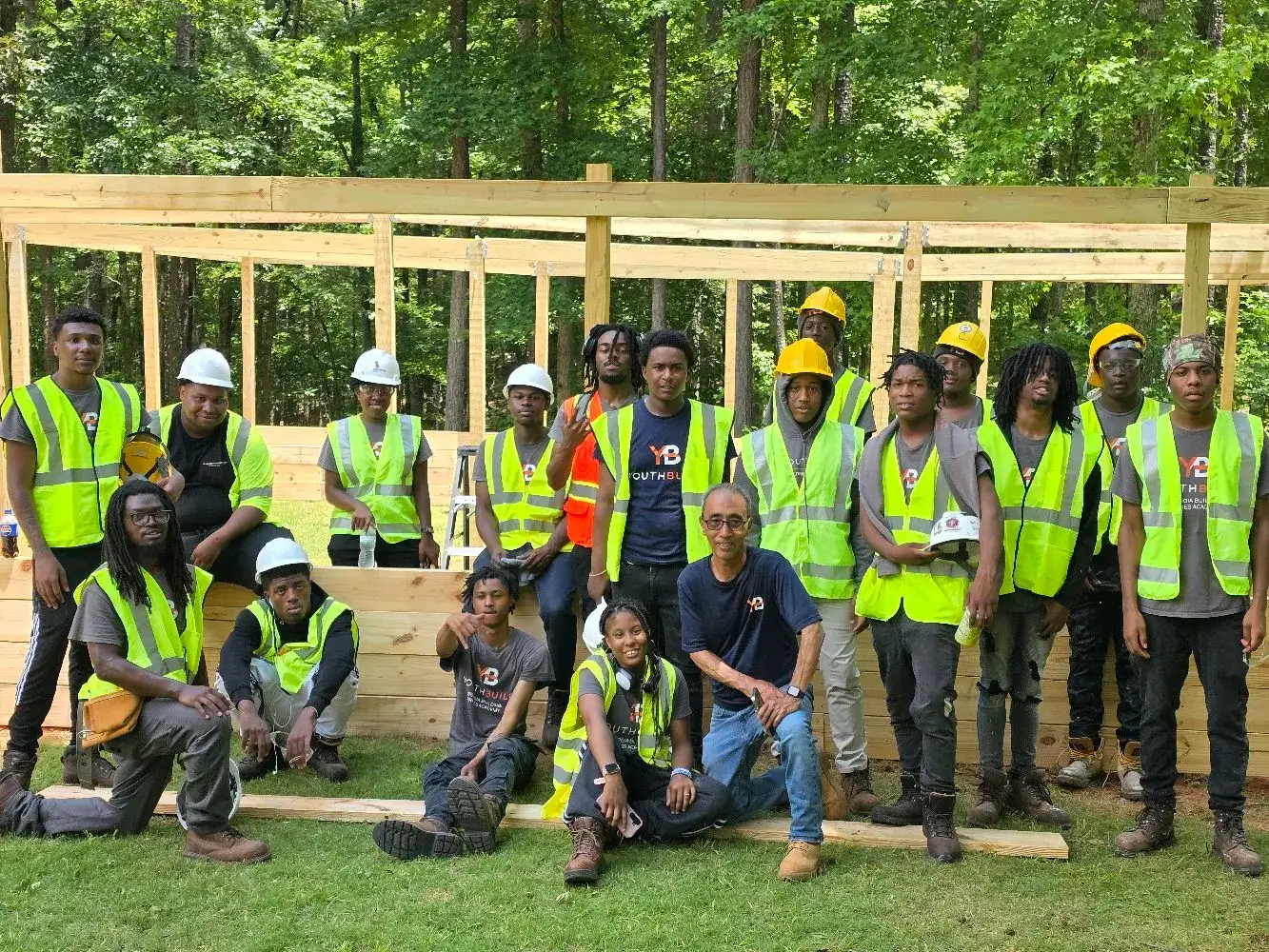 A YouthBuild cohort in hi-vis vests and hard hats in front of a wall they framed
