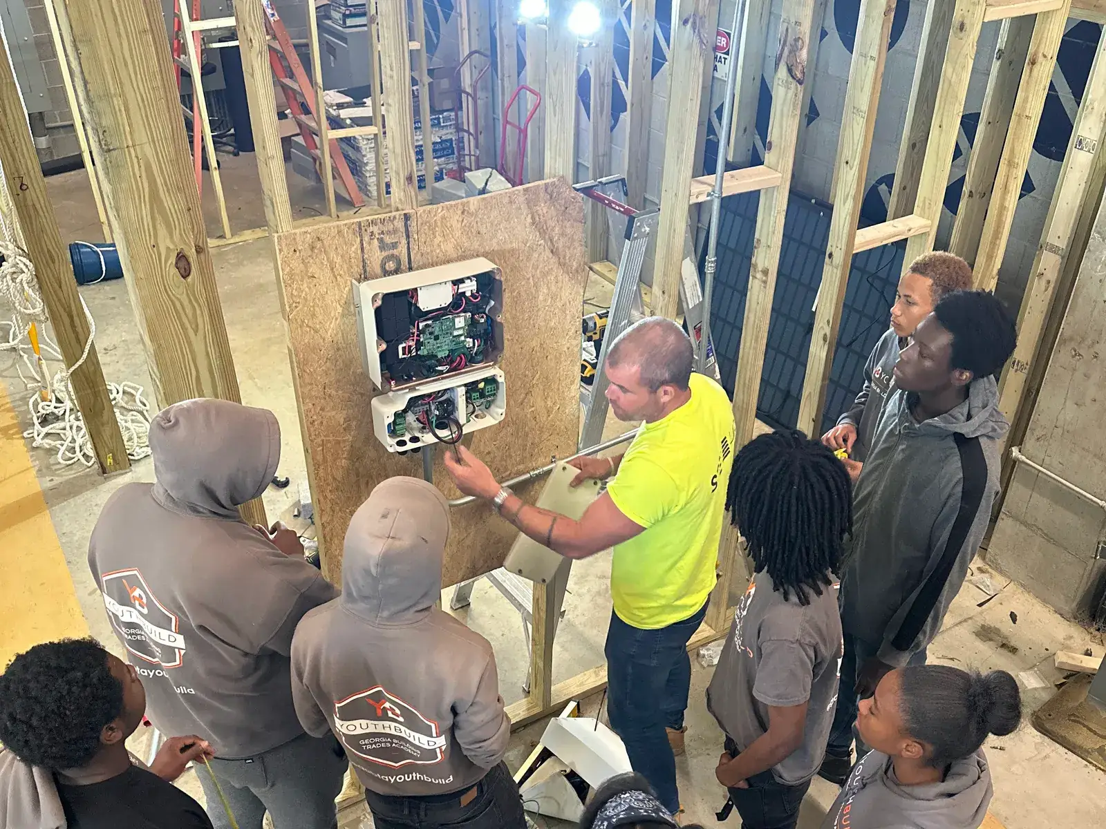 An instructor walks YouthBuild participants through an electrical panel in a framed wall