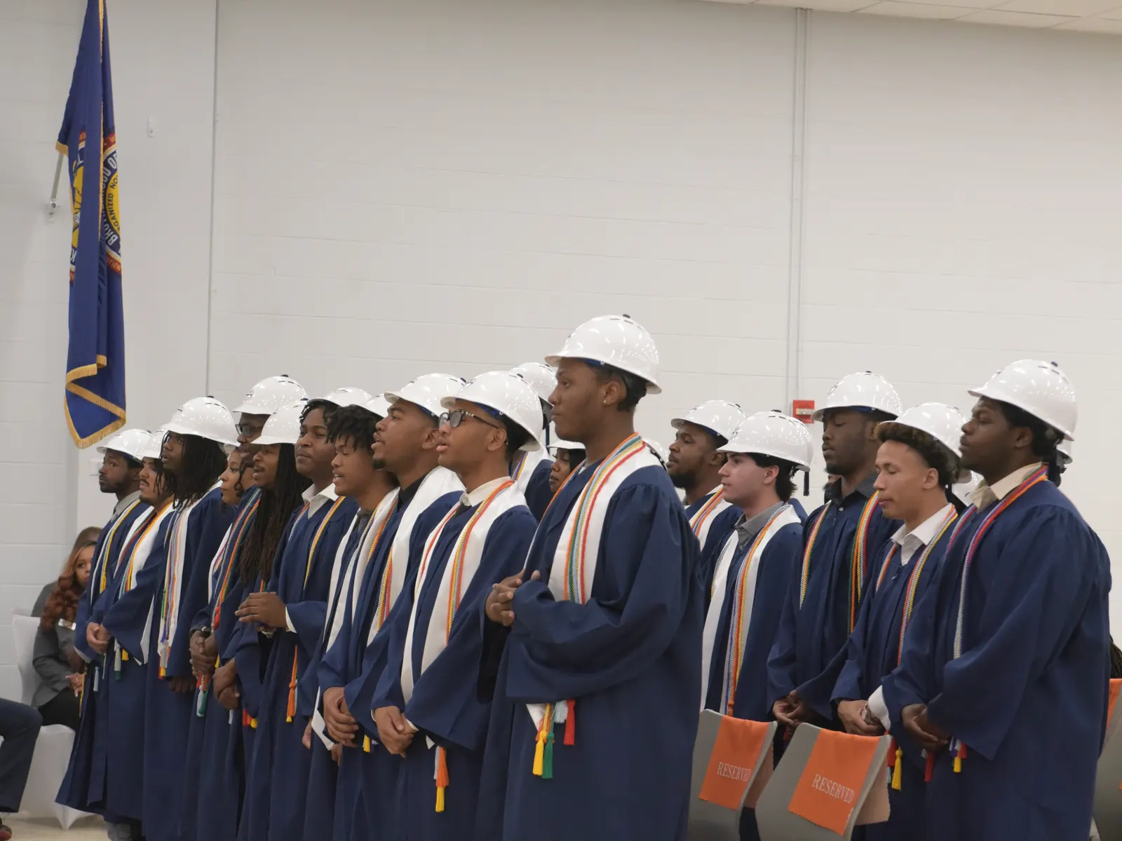 YouthBuild graduates lined up in caps, gowns, and hard hats at the ceremony