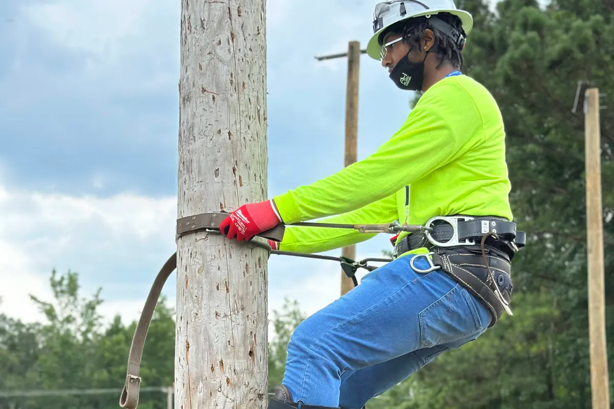 A participant in a harness and climbing hooks partway up a utility pole